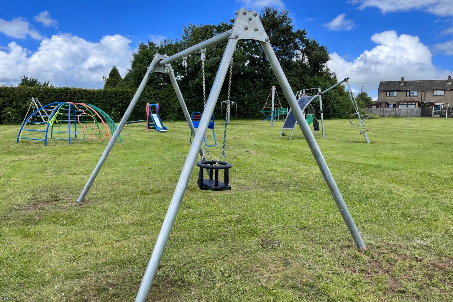 Metal swings set in a public playground on a grass field, suitable for parks, schools and community outdoor spaces