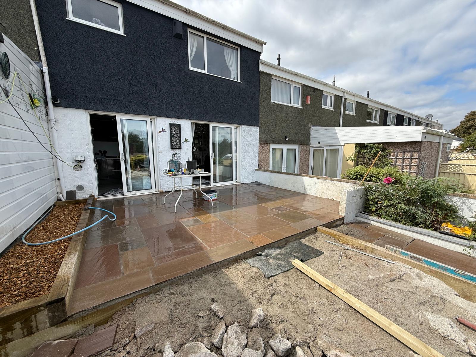 Indian sandstone paving patio installation in modern residential garden with steps and gravel border.